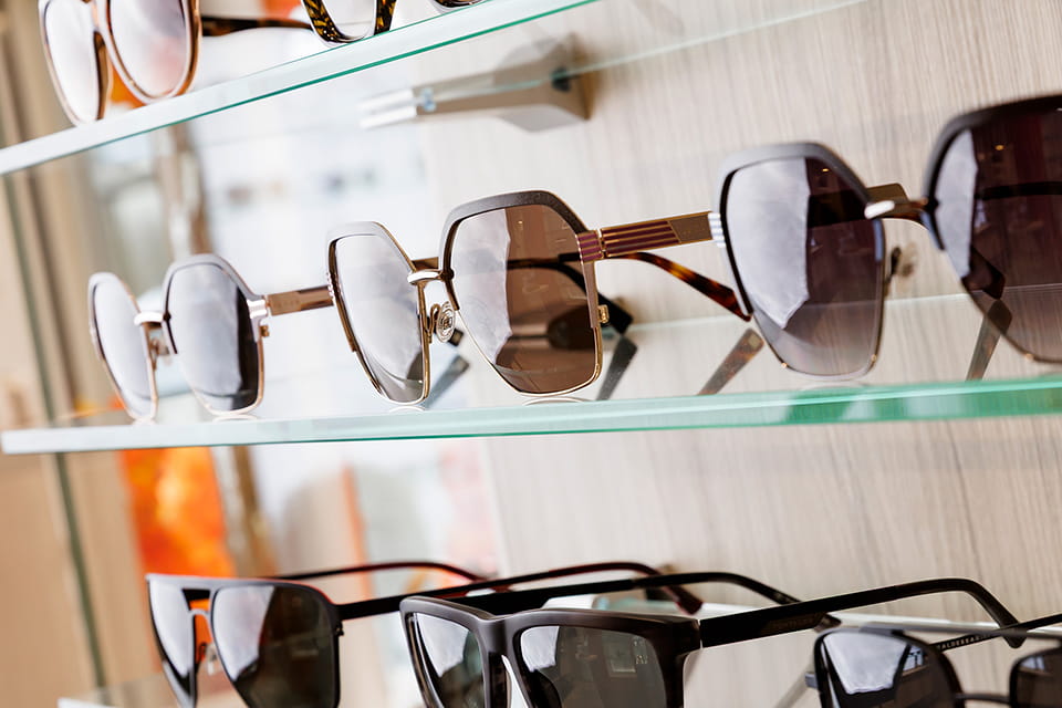 Sonnenbrillen mit getönten Gläsern auf Glasregalen im Fachgeschäft. Fokus auf goldene Oversize-Fassung